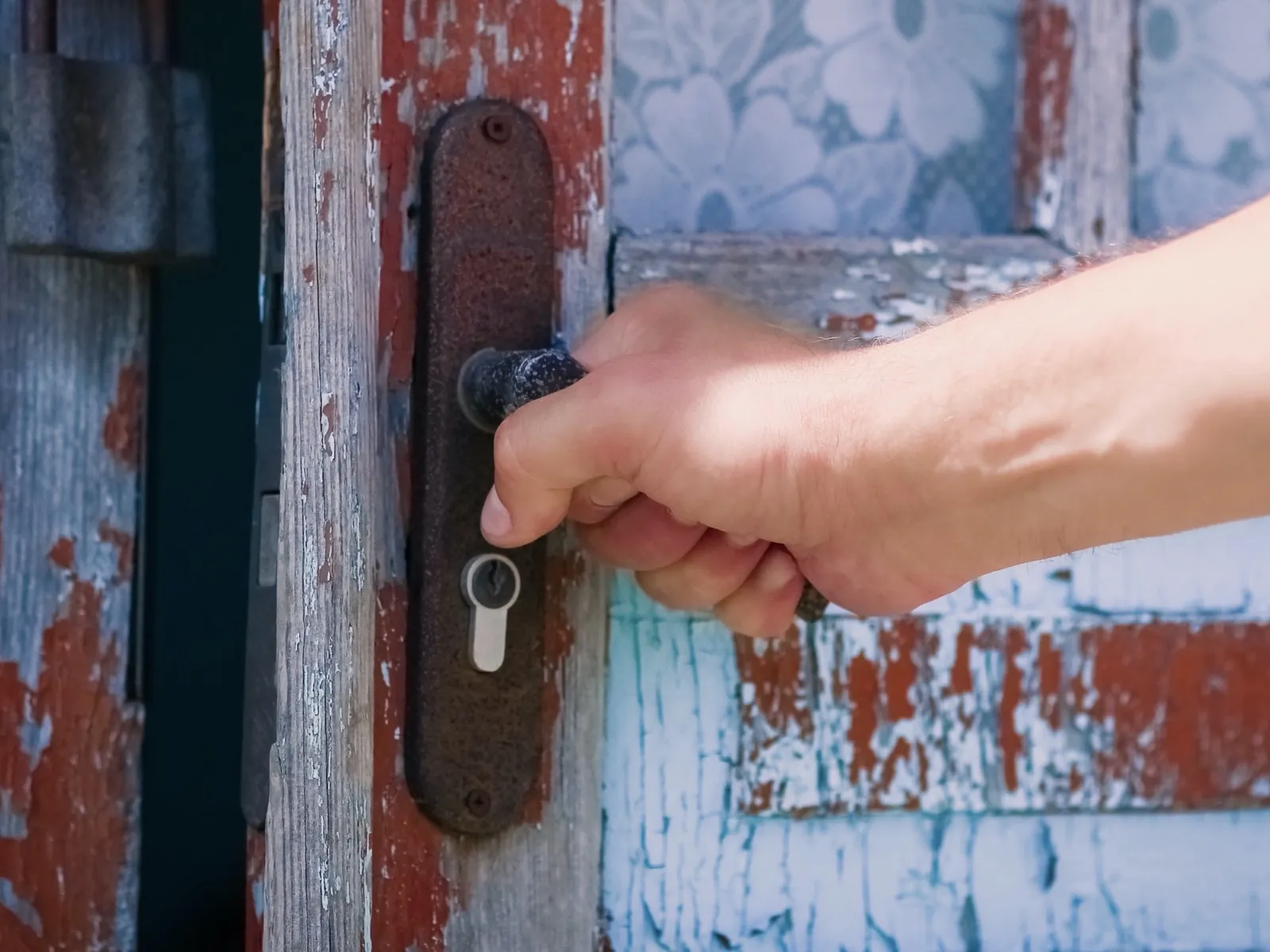 Une main sur la poignée-béquille d'une vieille porte à la peinture écaillée.